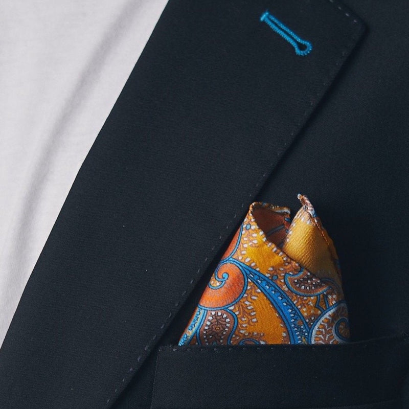 Silk square handkerchief presented in a ‘cone’ and placed in a suit jacket pocket, showing the gold and cyan colour combo.