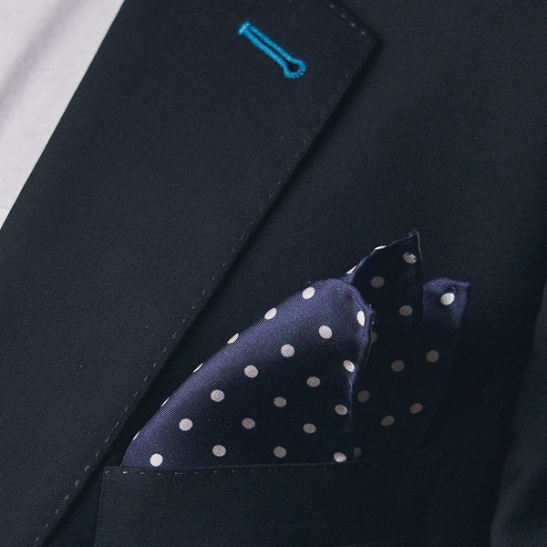 Silk square handkerchief presented in a ‘cone’ and placed in a suit jacket pocket, showing the navy-blue fabric complemented by small white dots.