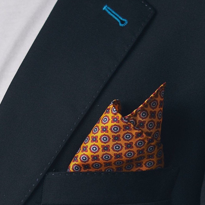 Silk square handkerchief presented in a ‘cone’ and placed in a suit jacket pocket, showing the bright, eye-catching golden fabric.